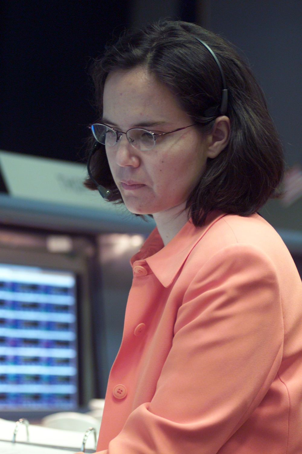 A person wearing eyeglasses and a coral cardigan looking down attentively.